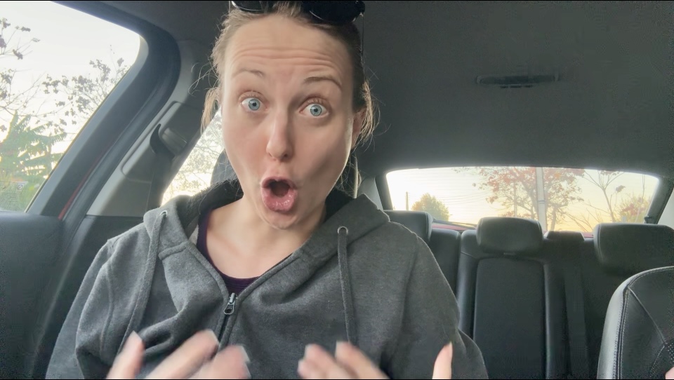 Woman sitting in the car with a hoodie on, her mouth open in the shape of the 'o' in 'no', eyebrows raised, wrinkled forehead looking scared and nervous.