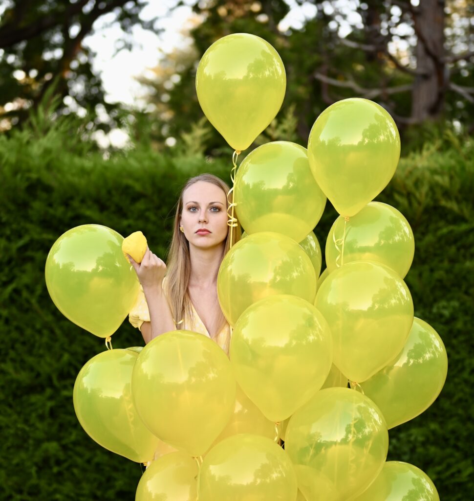 woman surrounded by yellow balloons for endometriosis, signifying ovaries or eggs. The woman is holding one deflated balloon showing how you have to advocate for yourself or we become squashed.