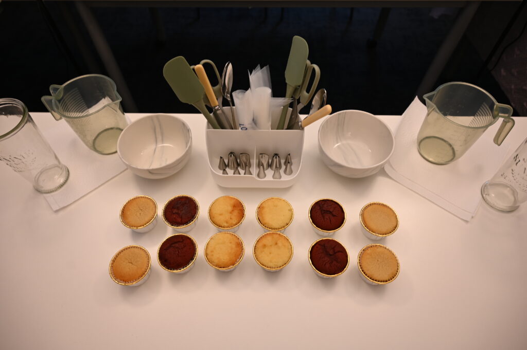 Close-up of a cupcake decorating station with piping bags, metal nibs, cupcake cases, and other decorating tools neatly arranged on a table.
